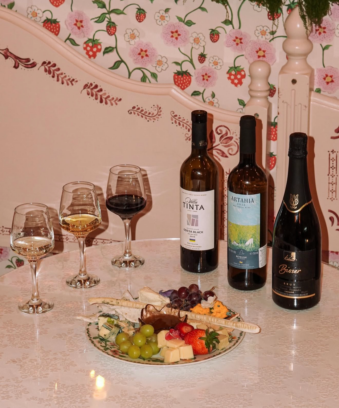 Wine and vegan cheese tasting with three bottles of wine, filled glasses and a plant-based cheeseboard with grapes and fruit.