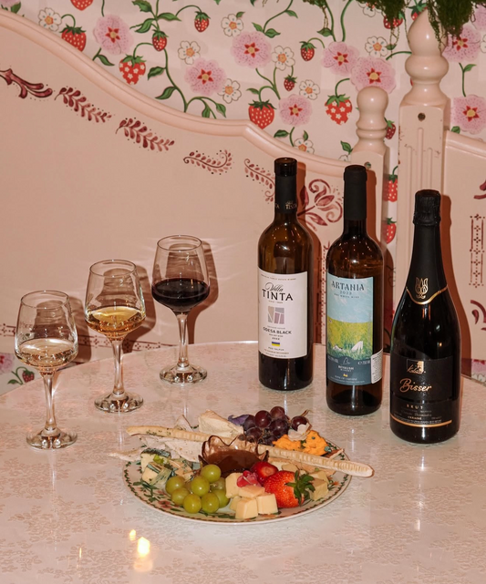 Wine and vegan cheese tasting with three bottles of wine, filled glasses and a plant-based cheeseboard with grapes and fruit.